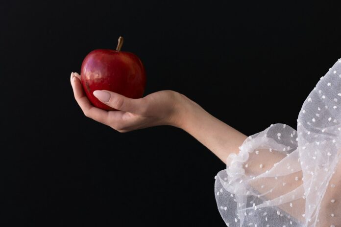 A woman in a white dress holding an apple