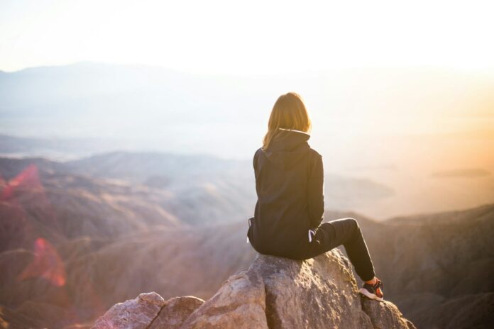 Photo by Denys Nevozhai person sitting on top of gray rock overlooking mountain during daytime
