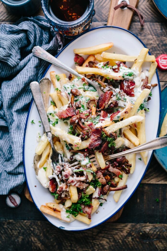 Photo by Brooke Lark bacon strips and melted cheese topped fries on oval white and blue platter with gray stainless steel forks