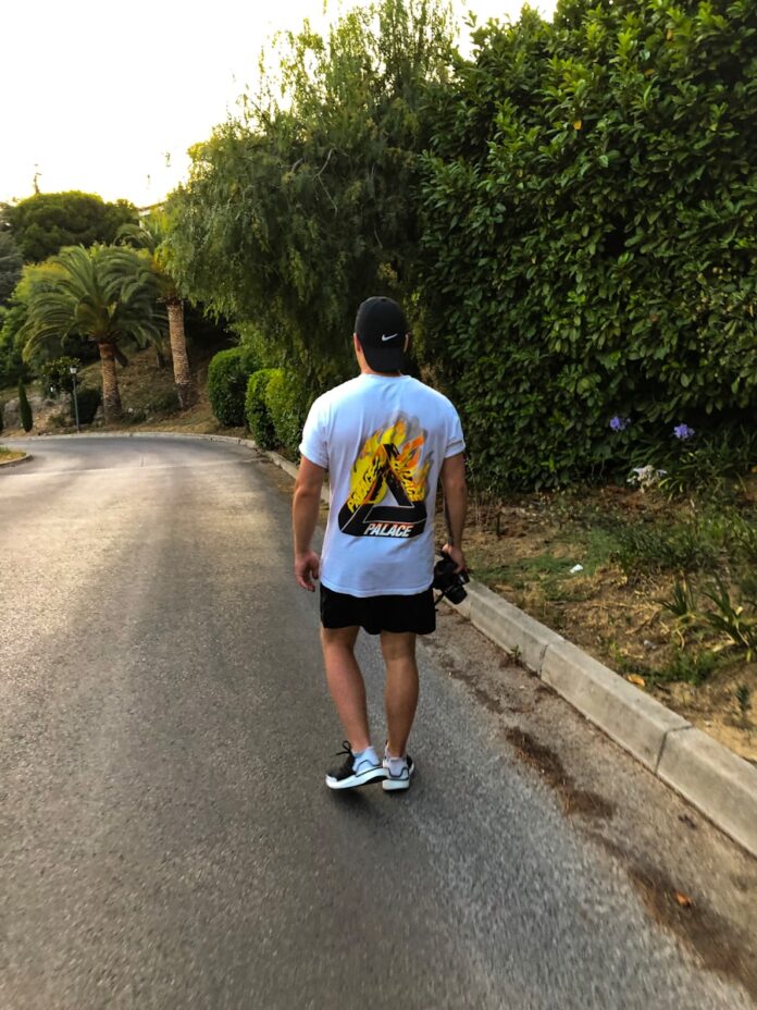 man walking on road beside trees